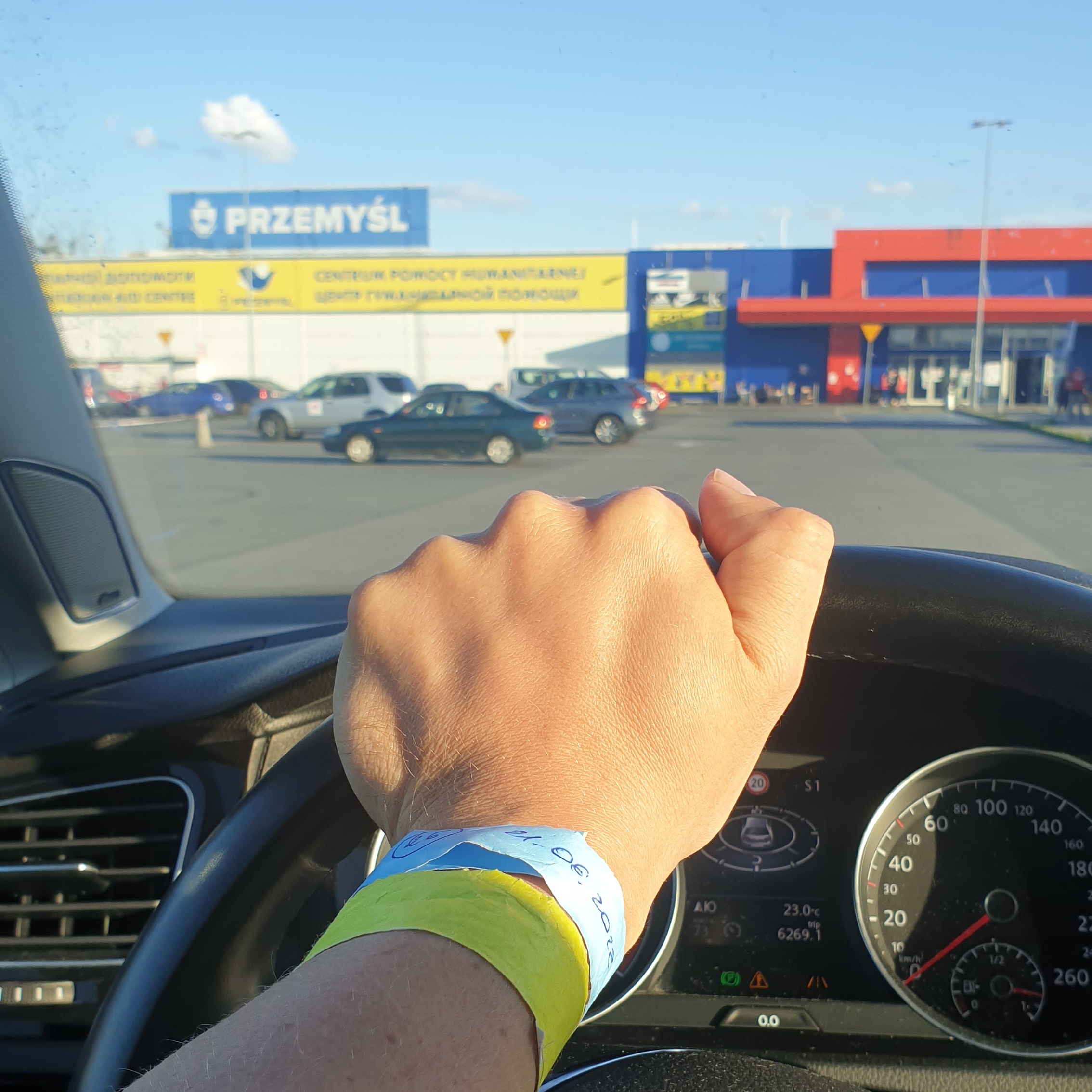 Вид из авто на центр помощи беженцам в Пшемысле; волонтерская идентификация на руке водителя.